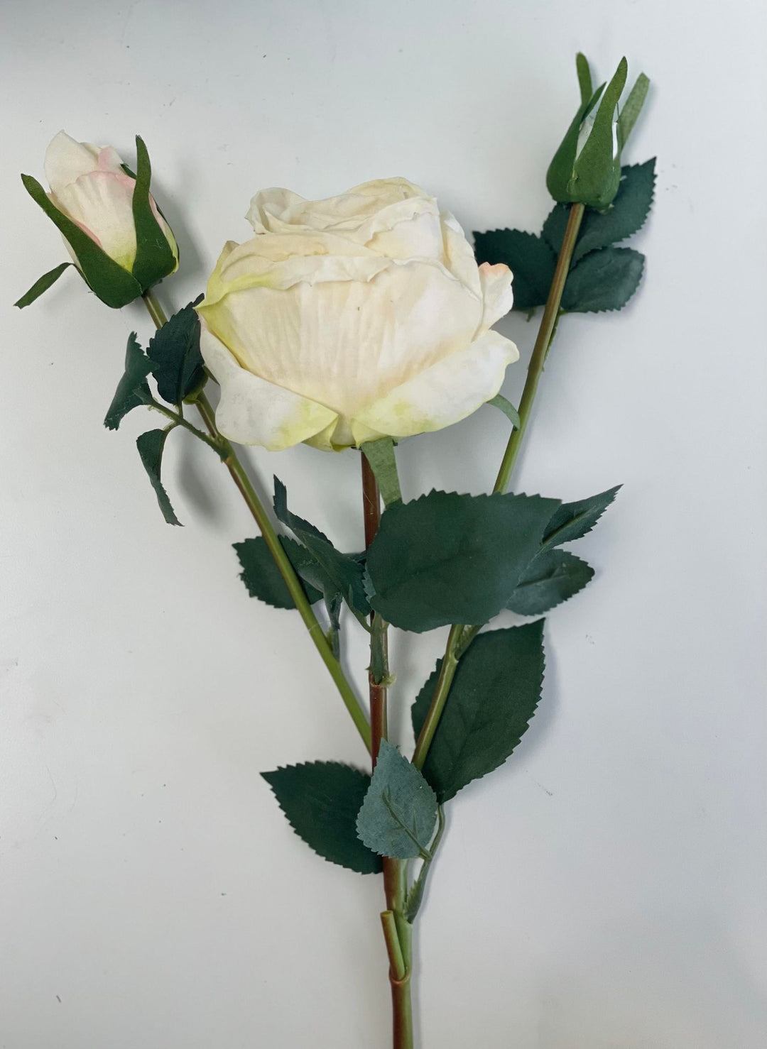  artificial white rose stems with green leaves against a white background. Common question: How can you make artificial roses look more realistic in floral arrangements?