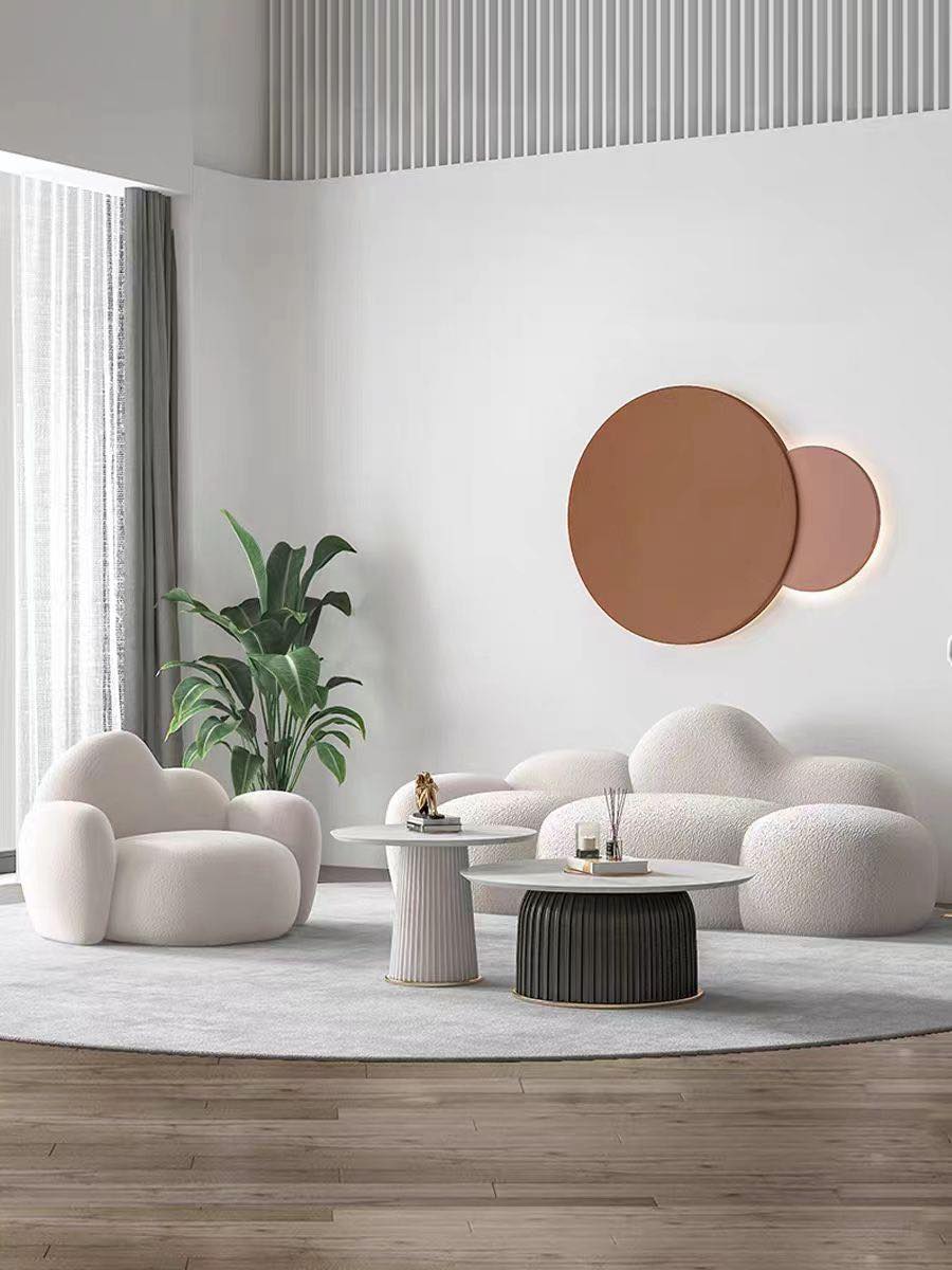 What are the best coffee tables for a cloud couch setup? This modern living room features a plush white cloud-shaped sofa and armchairs paired with two round marble-topped coffee tables. The tables have sleek gold accents and complement the soft, inviting furniture, creating a cozy and stylish atmosphere. A large plant and minimal décor enhance the contemporary design.