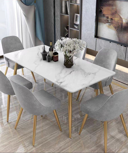 What are the best marble dining tables for a luxury home? This elegant dining room features a white marble table with sleek gold legs, paired with six gray velvet chairs that also have gold accents. The modern design, combined with luxurious materials, creates a sophisticated dining space perfect for contemporary interiors.