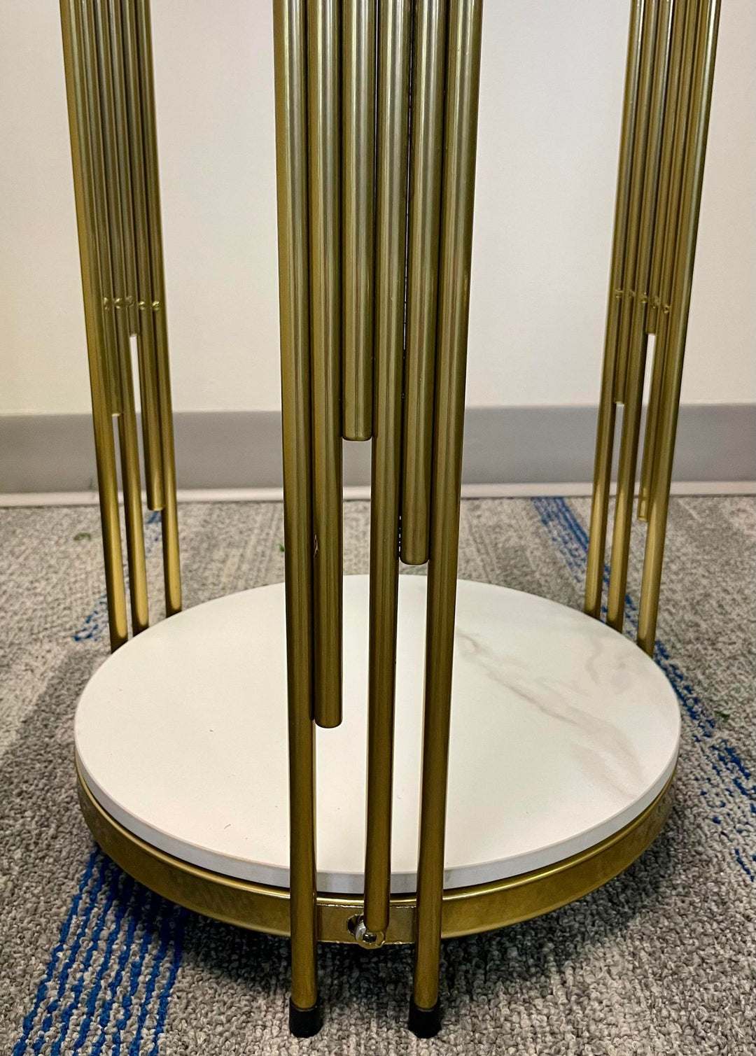 Close-up of a gold metal plant stand with a marble base, showcasing its sleek vertical rods design. How do I maintain a plant stand with a marble top to prevent damage?