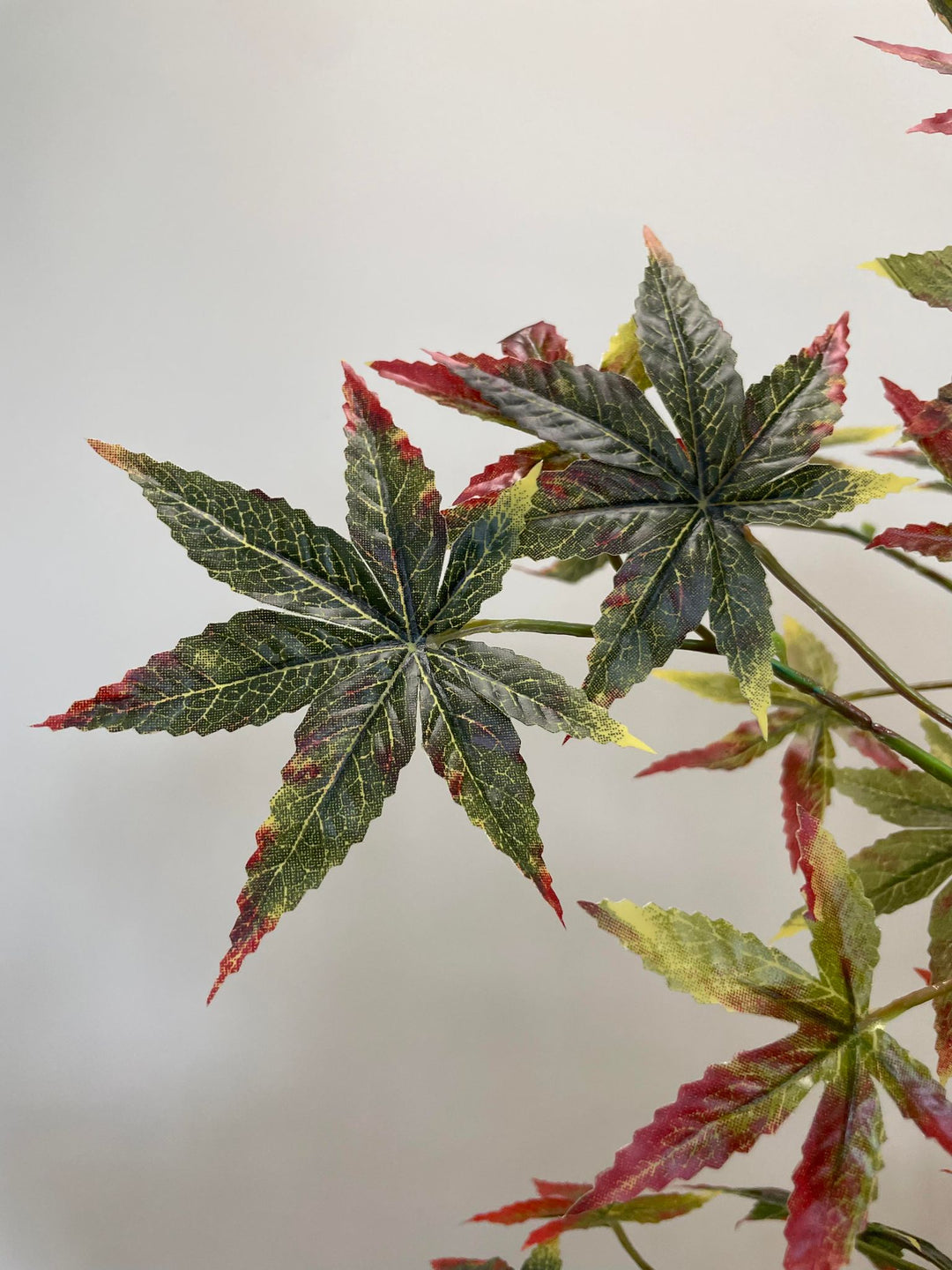 Close-up view of artificial Japanese maple tree leaves featuring a mix of dark green and vibrant red colors, showing detailed leaf veins and textures.