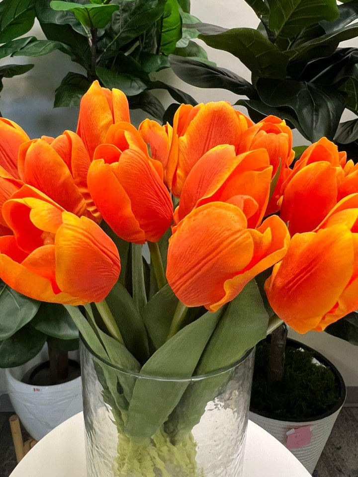 A delicate bouquet of artificial orange tulips displayed in a clear glass vase, set against a lush green background. How do I choose the right vase for displaying artificial flowers?