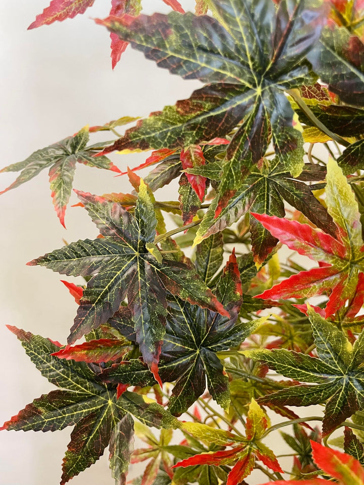 Close-up view of artificial Japanese maple tree leaves featuring a mix of dark green and vibrant red colors, showing detailed leaf veins and textures