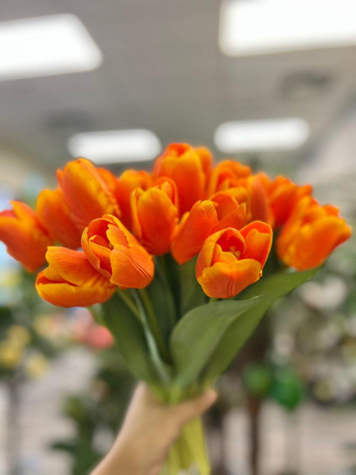 A vibrant bouquet of artificial orange tulips held by hand, with realistic petals and leaves. What are the best tips for choosing high-quality artificial flowers?