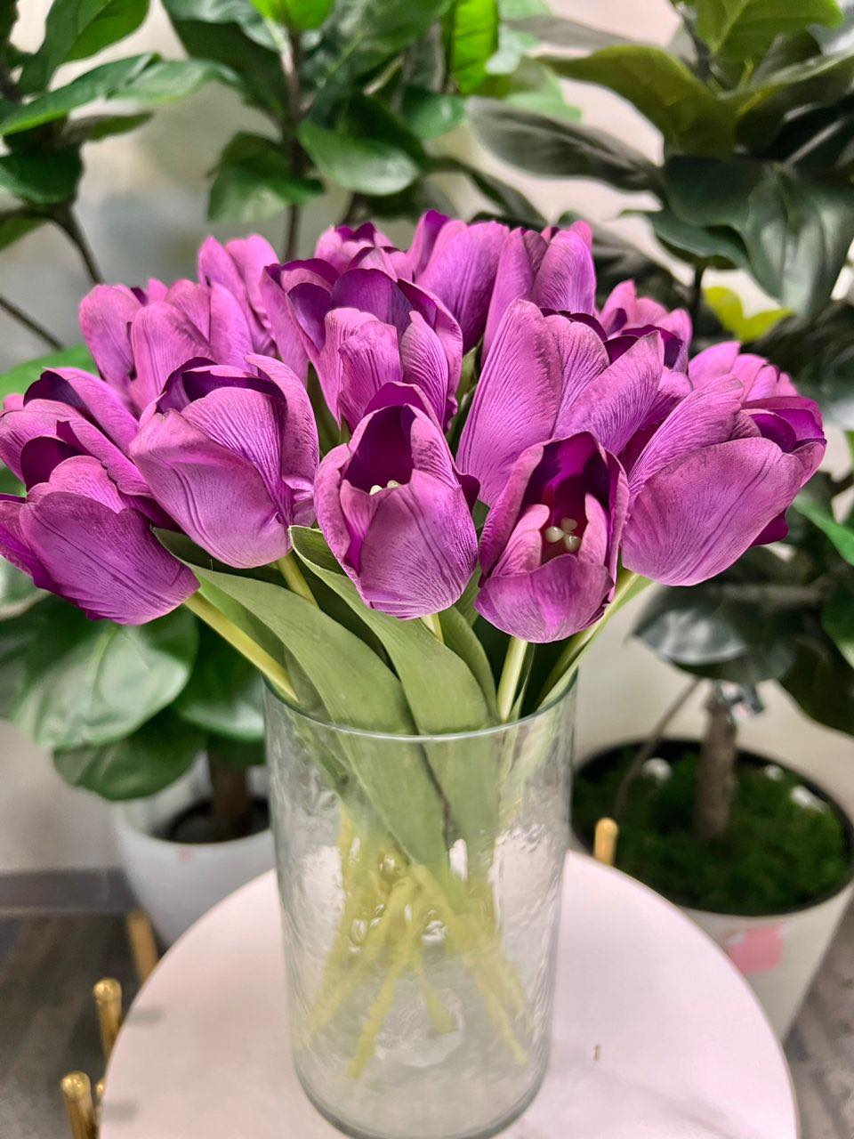 A delicate bouquet of artificial purple tulips displayed in a clear glass vase, set against a lush green background. How do I choose the right vase for displaying artificial flowers?