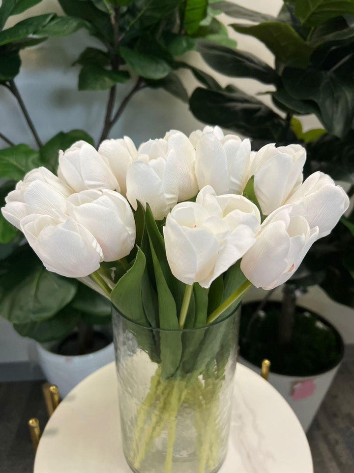 A delicate bouquet of artificial white tulips displayed in a clear glass vase, set against a lush green background. How do I choose the right vase for displaying artificial flowers?