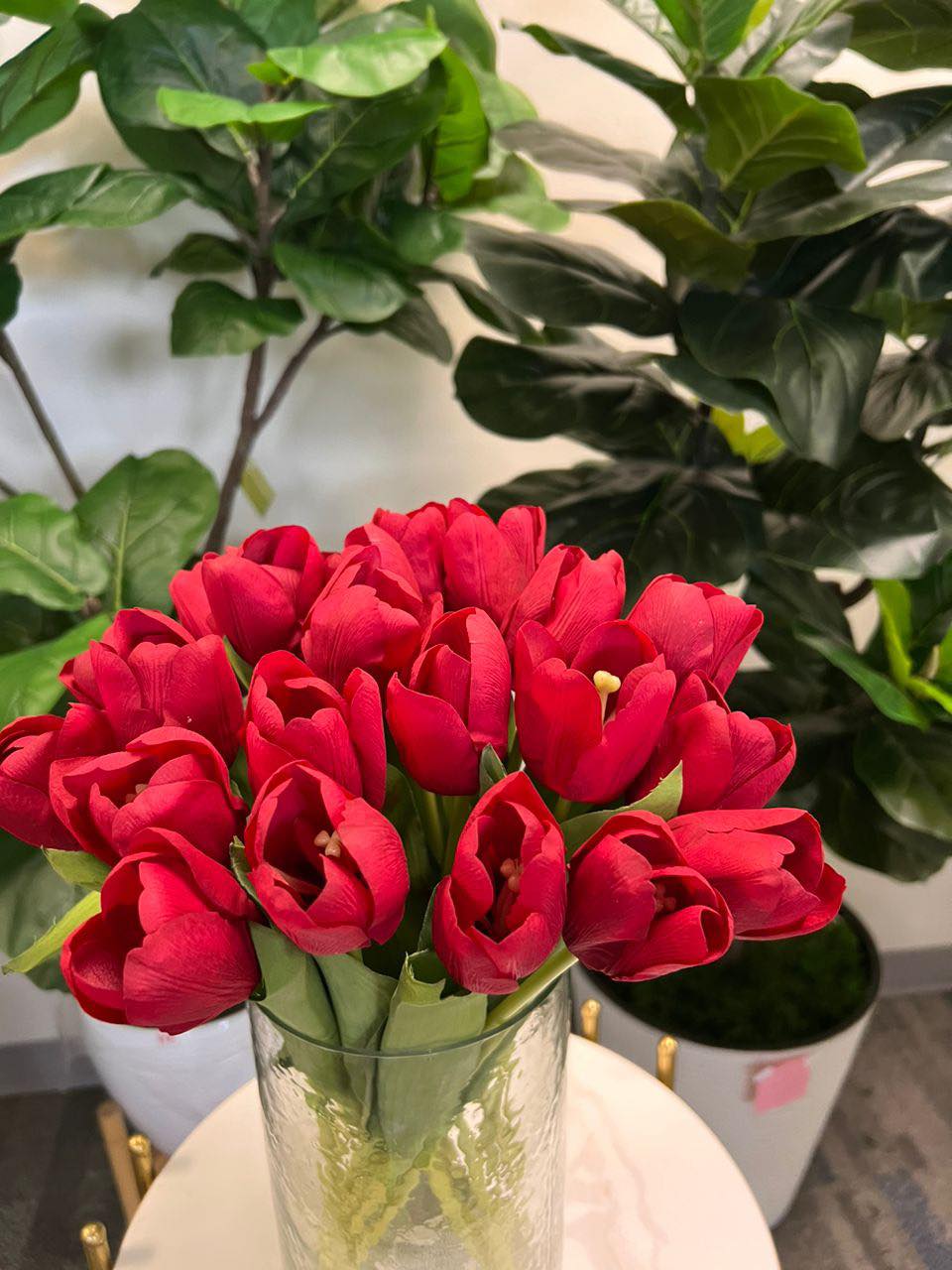 A delicate bouquet of artificial red tulips displayed in a clear glass vase, set against a lush green background. How do I choose the right vase for displaying artificial flowers?