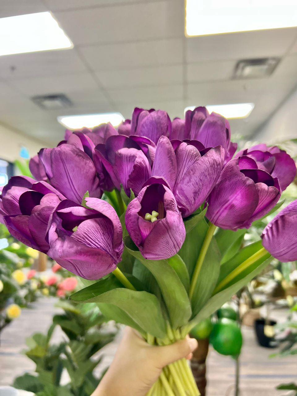 A vibrant bouquet of artificial purple tulips held by hand, with realistic petals and leaves. What are the best tips for choosing high-quality artificial flowers?