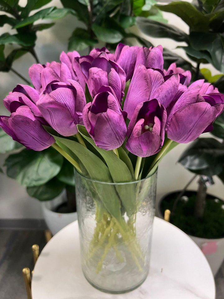 A delicate bouquet of artificial purple tulips displayed in a clear glass vase, set against a lush green background. How do I choose the right vase for displaying artificial flowers?
