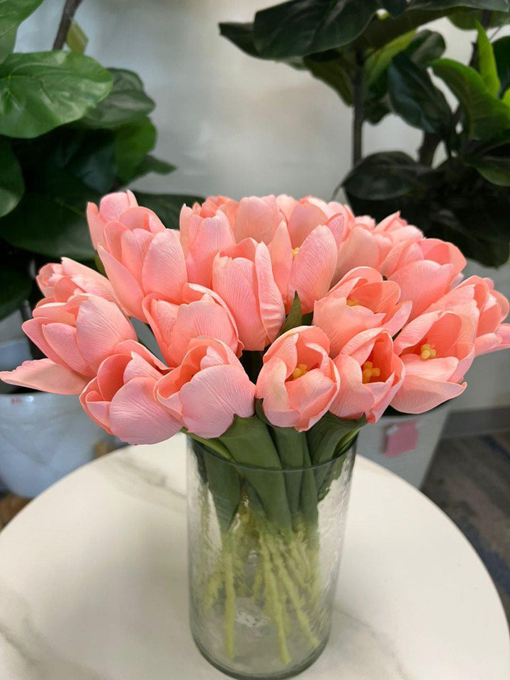 A delicate bouquet of artificial pink tulips displayed in a clear glass vase, set against a lush green background. How do I choose the right vase for displaying artificial flowers?