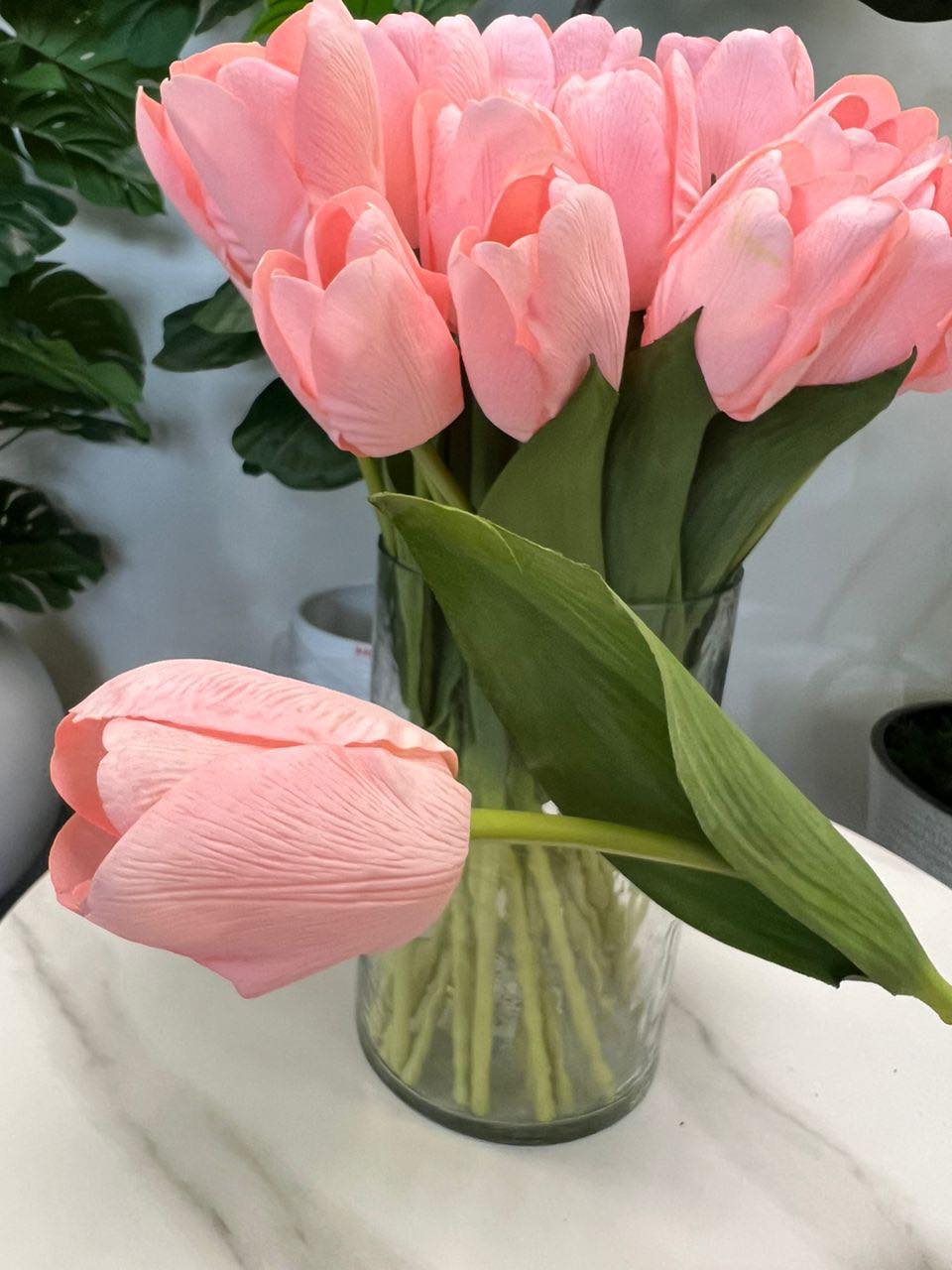 A delicate bouquet of artificial pink tulips displayed in a clear glass vase, set against a lush green background. How do I choose the right vase for displaying artificial flowers?