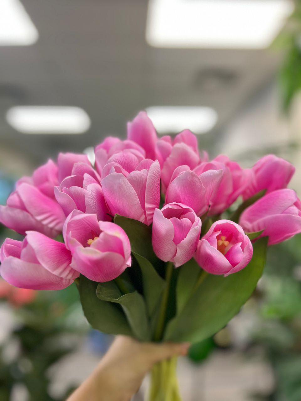 A vibrant bouquet of artificial pink tulips held by hand, with realistic petals and leaves. What are the best tips for choosing high-quality artificial flowers?