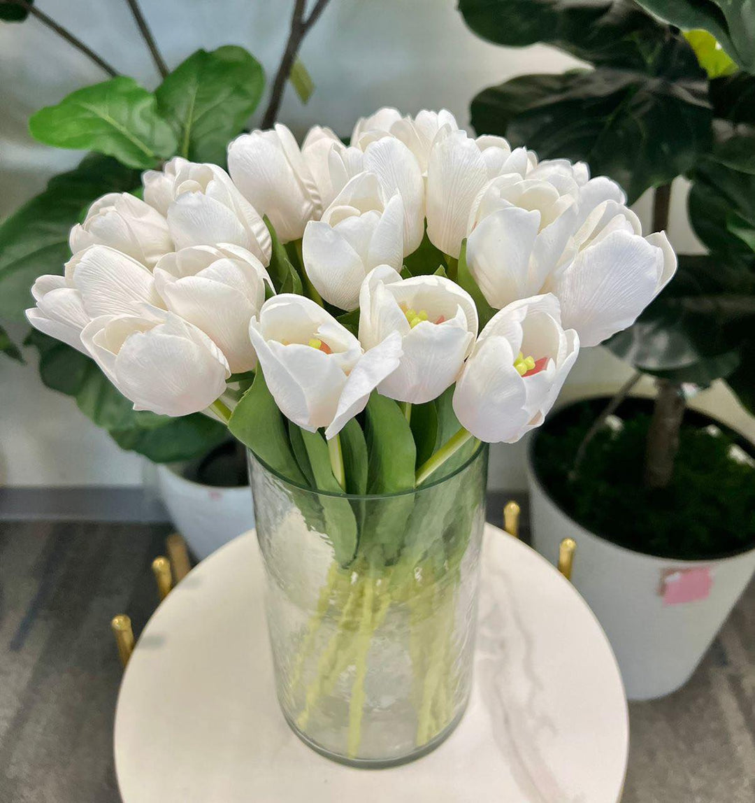 A delicate bouquet of artificial white tulips displayed in a clear glass vase, set against a lush green background. How do I choose the right vase for displaying artificial flowers?