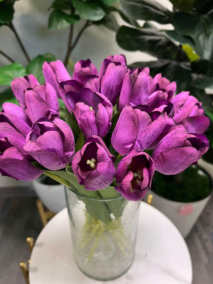 A delicate bouquet of artificial purple tulips displayed in a clear glass vase, set against a lush green background. How do I choose the right vase for displaying artificial flowers?