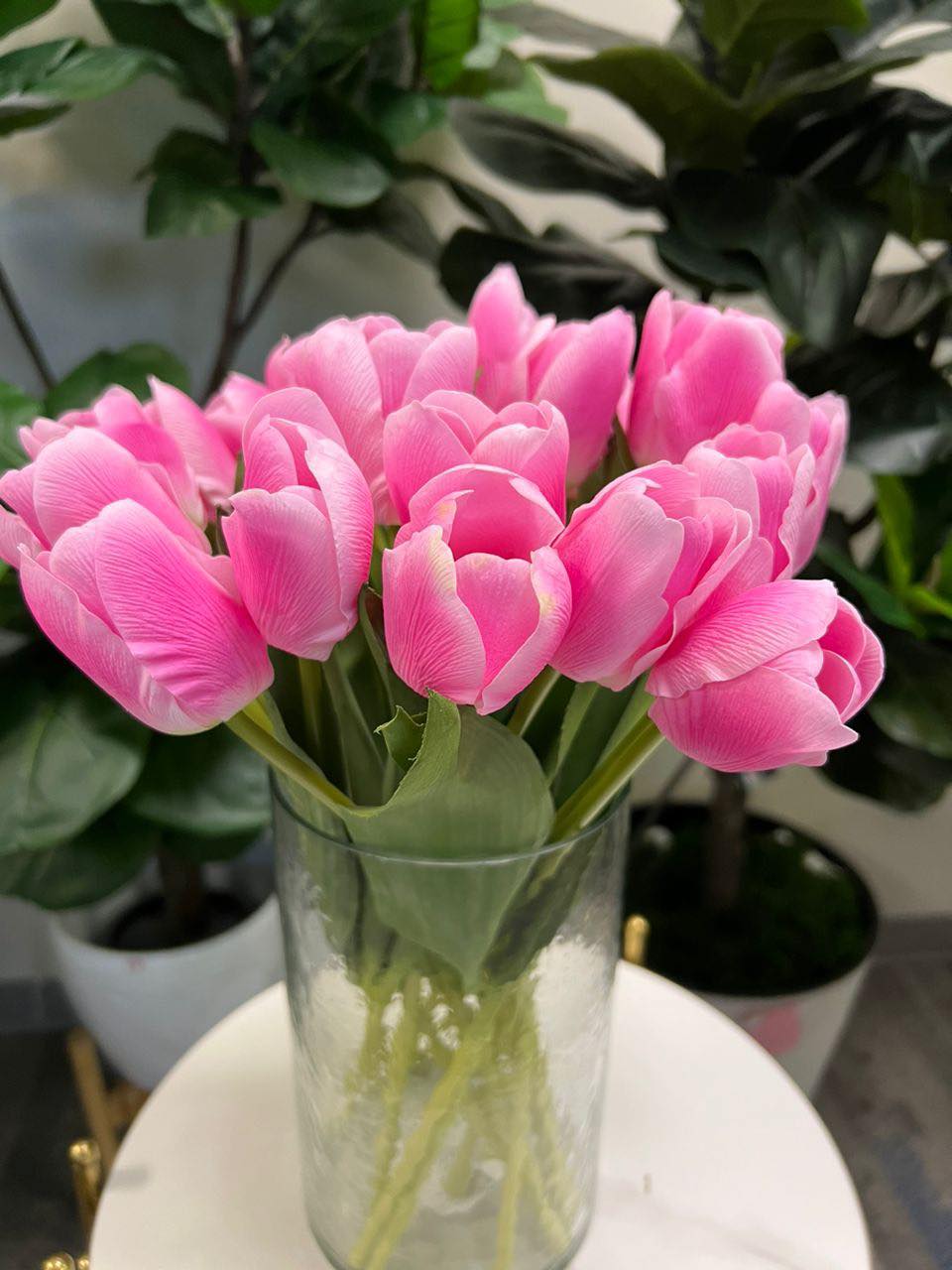 A delicate bouquet of artificial pink tulips displayed in a clear glass vase, set against a lush green background. How do I choose the right vase for displaying artificial flowers?