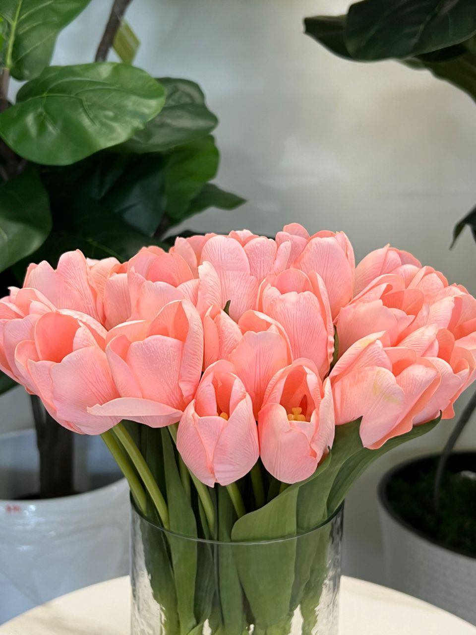 A delicate bouquet of artificial pink tulips displayed in a clear glass vase, set against a lush green background. How do I choose the right vase for displaying artificial flowers?