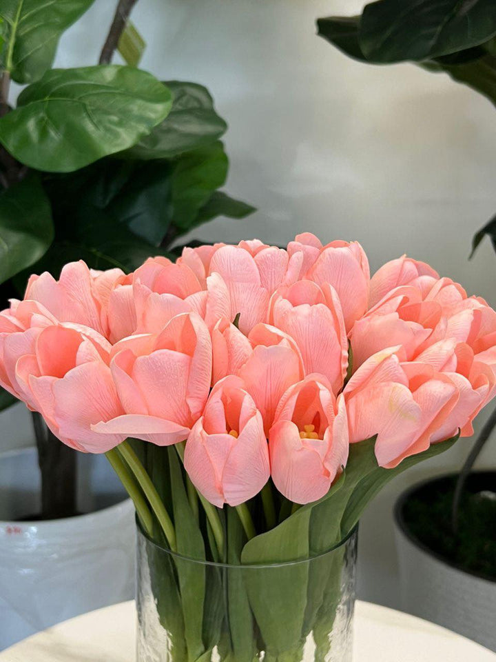 A delicate bouquet of artificial pink tulips displayed in a clear glass vase, set against a lush green background. How do I choose the right vase for displaying artificial flowers?