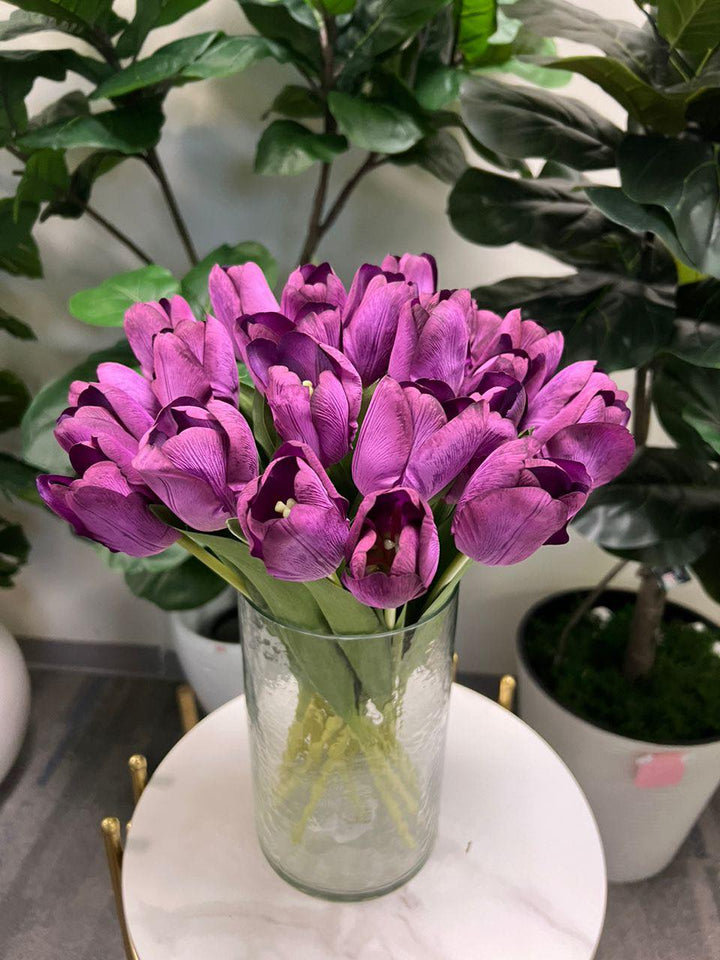 A delicate bouquet of artificial purple tulips displayed in a clear glass vase, set against a lush green background. How do I choose the right vase for displaying artificial flowers?
