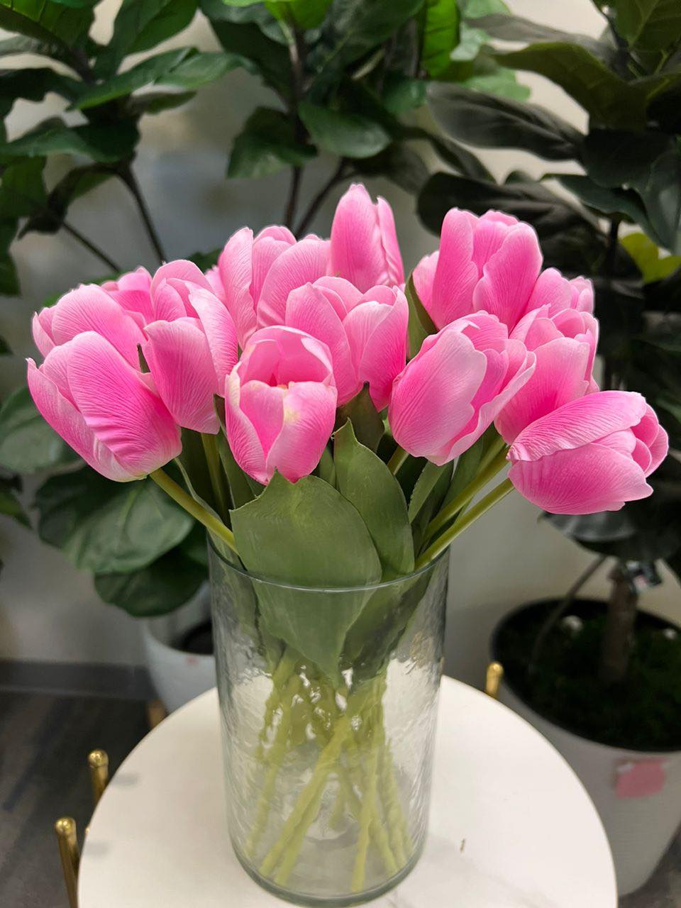 A delicate bouquet of artificial pink tulips displayed in a clear glass vase, set against a lush green background. How do I choose the right vase for displaying artificial flowers?