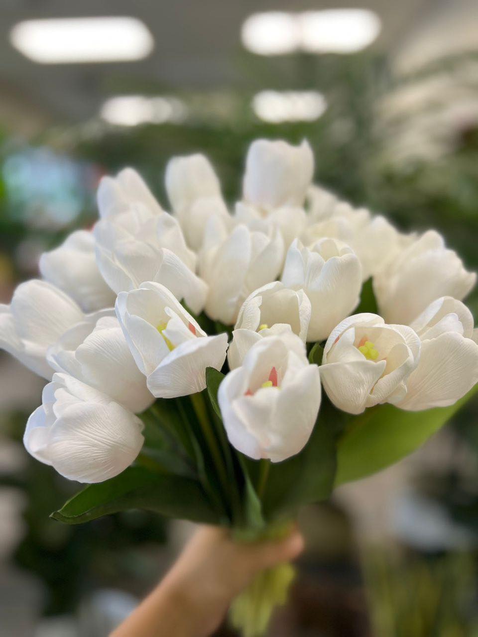 A vibrant bouquet of artificial white tulips held by hand, with realistic petals and leaves. What are the best tips for choosing high-quality artificial flowers?