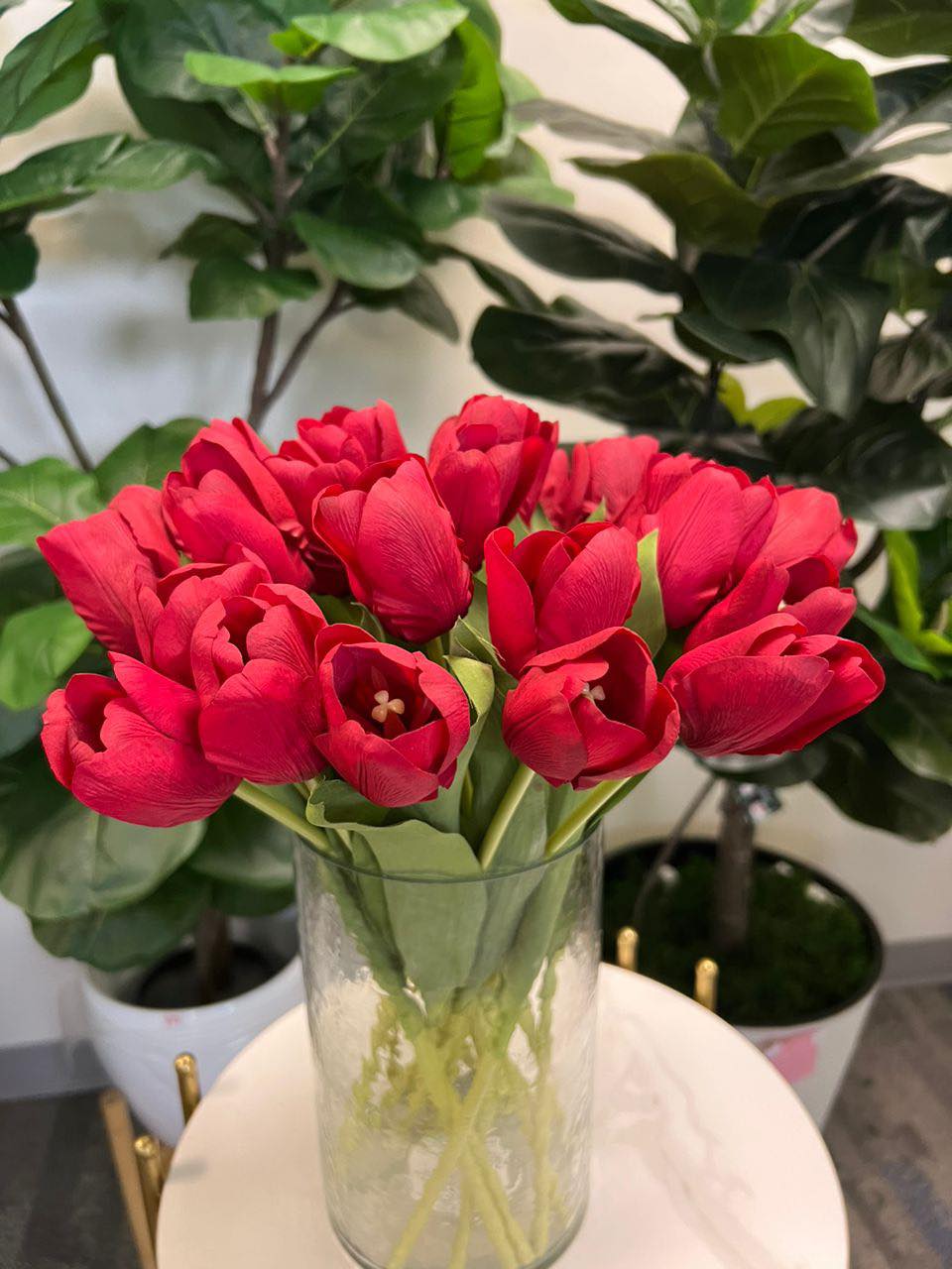 A delicate bouquet of artificial red tulips displayed in a clear glass vase, set against a lush green background. How do I choose the right vase for displaying artificial flowers?