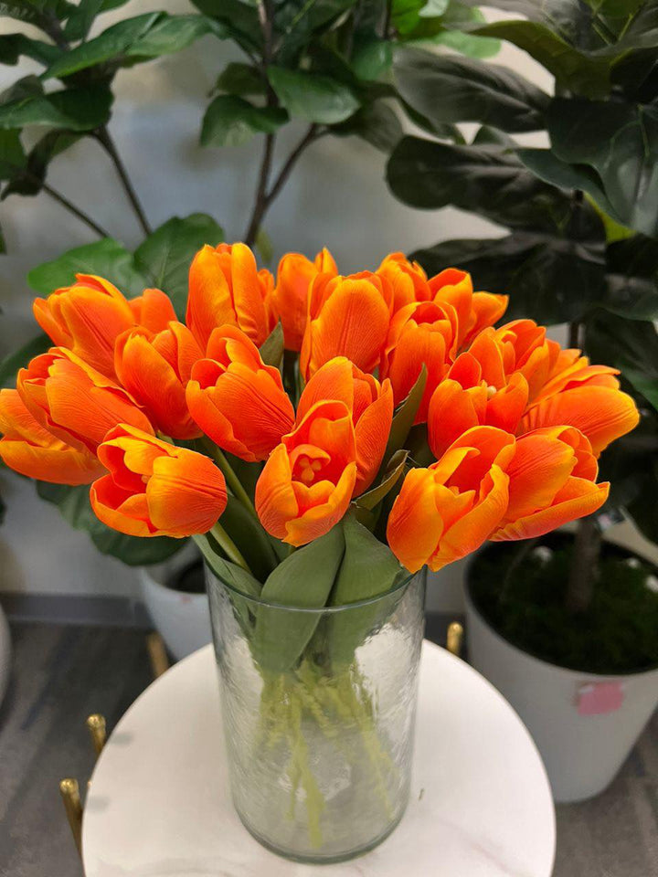 A delicate bouquet of artificial orange tulips displayed in a clear glass vase, set against a lush green background. How do I choose the right vase for displaying artificial flowers?