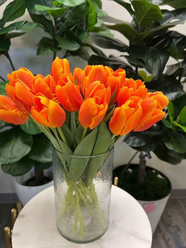 A delicate bouquet of artificial orange tulips displayed in a clear glass vase, set against a lush green background. How do I choose the right vase for displaying artificial flowers?