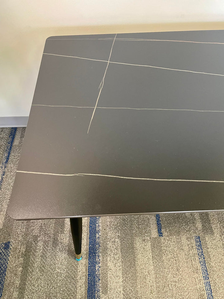 Close-up view of a modern black dining table with subtle light-colored veining, showcasing a minimalist and sleek design. The clean lines and smooth surface make it ideal for contemporary dining or workspace environments.
