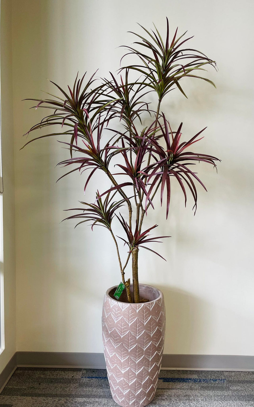 Artificial Dracaena plant with vibrant red-tinted leaves in a decorative pink geometric-patterned planter. This modern faux plant adds a touch of color and elegance to interior spaces, perfect for enhancing home or office decor.