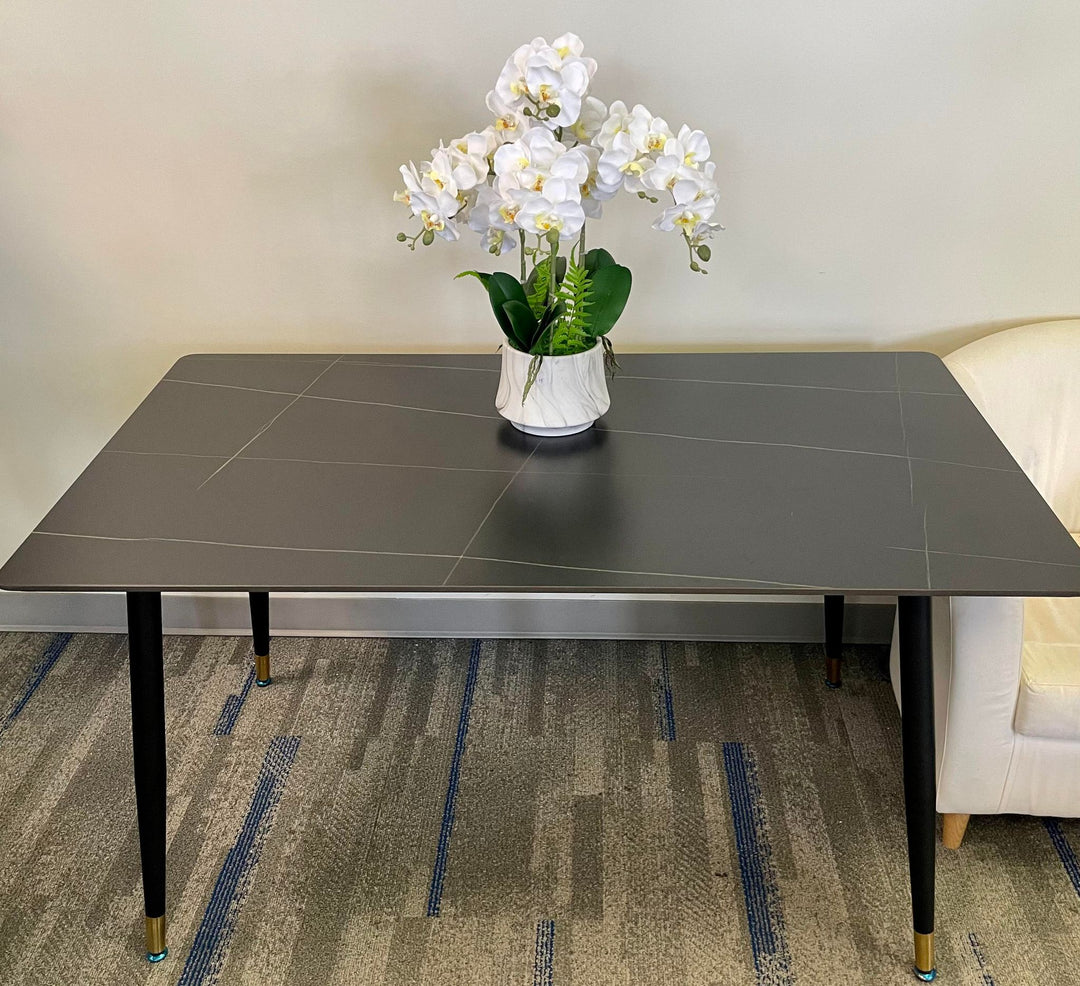 What are the best simple yet elegant dining tables? This minimalist black dining table with gold-accented legs is styled with a white orchid centerpiece, creating a clean and sophisticated look. The table's sleek design makes it perfect for modern dining spaces or home offices.