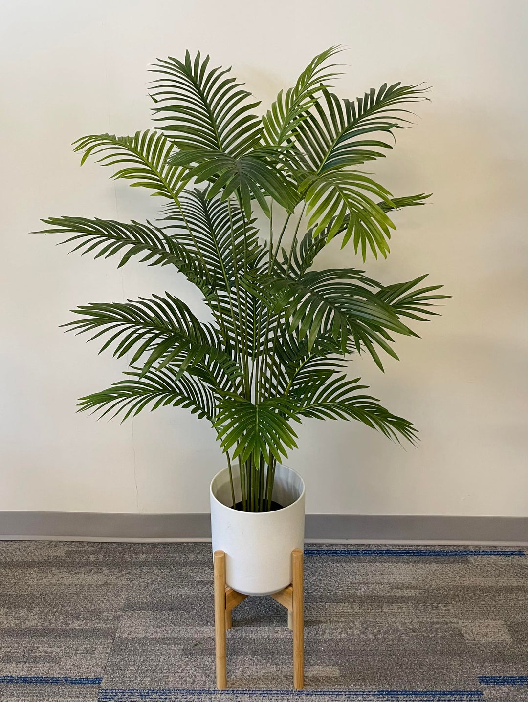 Modern office decor with a vibrant green palm plant in a sleek white planter, elevated on a wooden stand against a neutral wall.