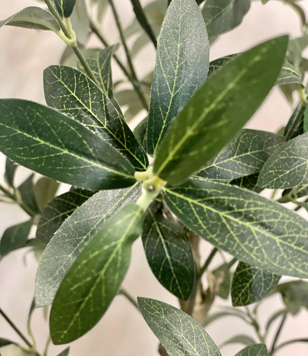Close-up image of artificial olive tree leaves, highlighting the intricate vein patterns and realistic texture against a neutral backdrop.