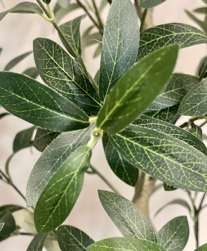 Close-up of artificial olive tree leaves, showcasing the detailed veining and texture of the green foliage, with a few black olives visible in the background.