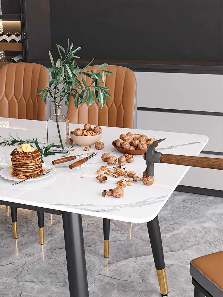 How durable are marble dining tables? This white marble dining table is shown being used to crack open walnuts with a hammer, showcasing its strength and durability. The table is paired with stylish tan upholstered chairs with gold accents, creating a modern and elegant dining space. Decorative items like pancakes and a vase with greenery add a cozy touch.