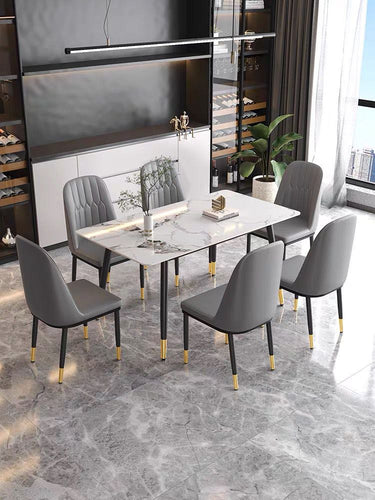 What is the best dining table for a modern home? This sleek dining room features a white marble table with black legs and gold accents, surrounded by six gray upholstered chairs with matching gold accents. The room is styled with built-in shelving, a wine storage area, and large windows that allow natural light to enhance the luxurious atmosphere.