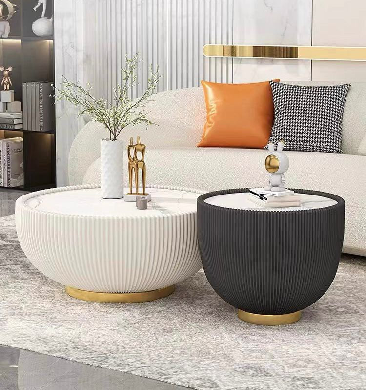 What are the best modern coffee tables for a living room? This stylish setup features two ribbed round coffee tables—one white and one black—with elegant gold bases. The tables are decorated with minimalistic items and placed in front of a cozy white sofa with accent pillows, combining functionality and style for a contemporary living room.