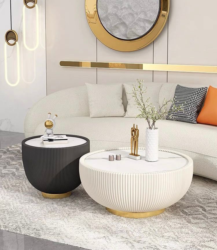 What are the most popular coffee table designs for modern homes? This living room features two round ribbed coffee tables, one in black and one in white, both with gold bases. They complement a curved white sofa with accent pillows, creating a luxurious and contemporary atmosphere. The tables are decorated with minimalistic vases and sculptures, adding both style and functionality to the space.