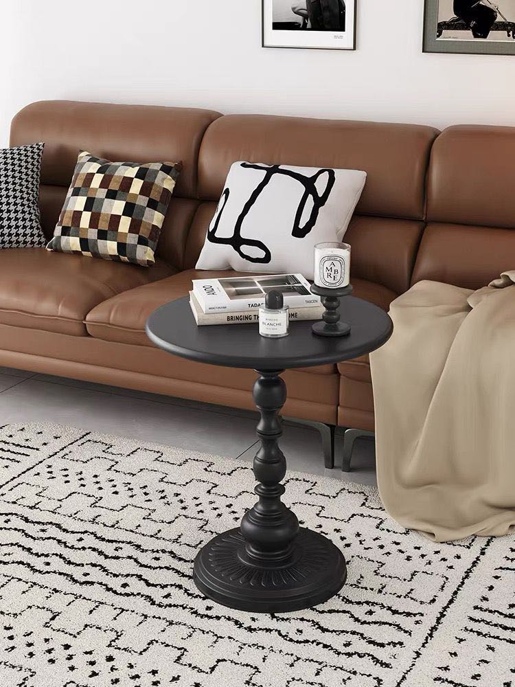 A small, black round side table with a decorative pedestal base is placed next to a light-colored sofa in a cozy room. 
