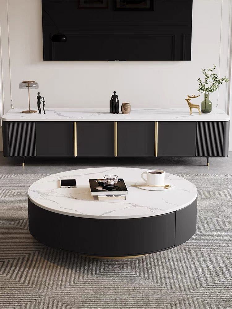 Modern living room with a round coffee table featuring a white marble top and black base. The table is placed on a geometric-patterned rug and in front of a sleek black TV stand with gold accents. Decorative items, including a lamp and sculptures, are arranged on the TV stand, creating a minimalist and sophisticated space
