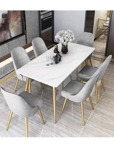 What are the best dining table sets for a modern kitchen? This sleek dining room setup features a white marble table with gold legs, surrounded by six gray velvet chairs, also with gold legs. The minimalist design creates a luxurious and contemporary feel, perfect for modern interiors.