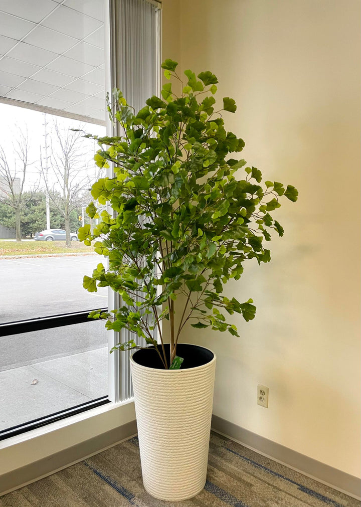 Artificial ginkgo tree in a tall white planter placed near a large window, bringing a touch of greenery and elegance to the indoor space.