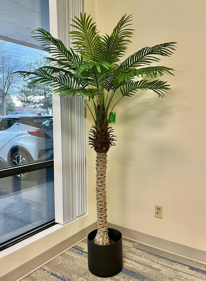 A large artificial palm tree in a stylish office corner by the window, adding a natural touch to a professional setting.