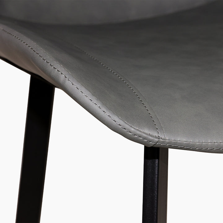 Close-up detail of a dark gray faux leather dining chair seat with fine stitching. Common questions include 'What material is best for dining chair upholstery?' and 'How do you clean faux leather dining chairs?