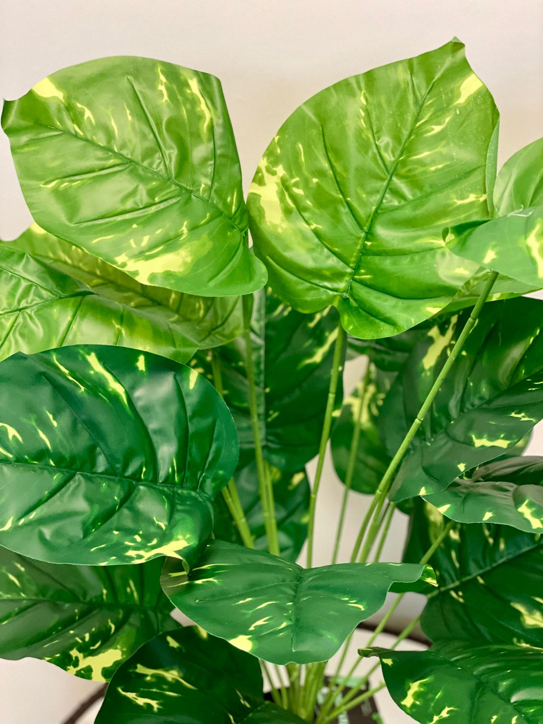 Close-up of artificial plant leaves showing vibrant green tones with yellow variegation, creating a lush, tropical look. The leaves appear glossy and healthy, giving the plant a realistic appearance.