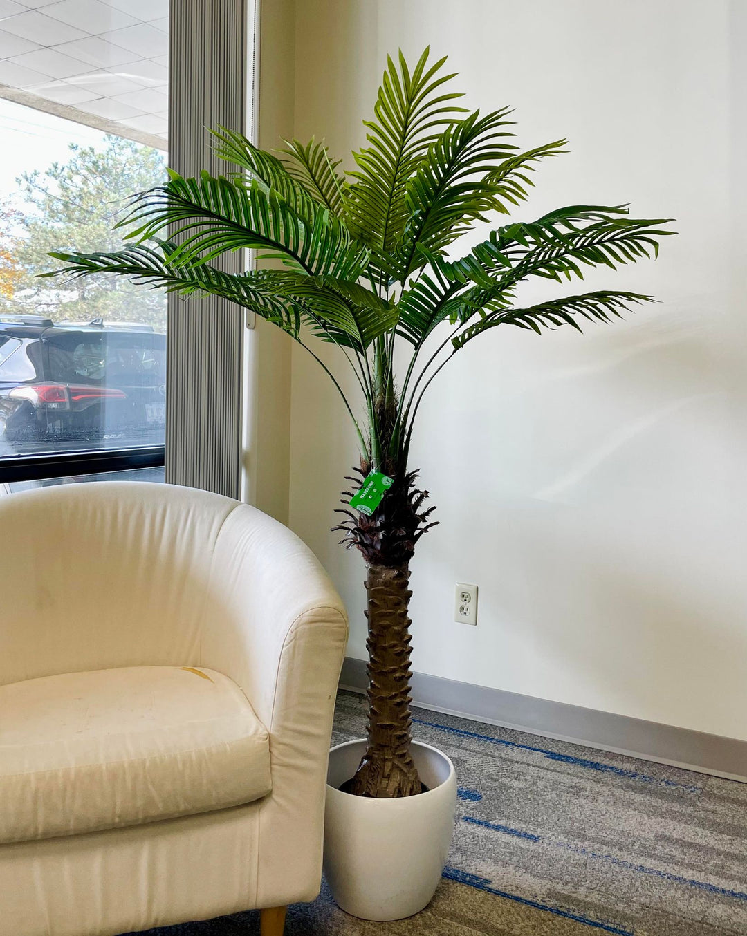 Realistic artificial palm tree placed next to a beige chair, bringing natural vibes to any interior design space.