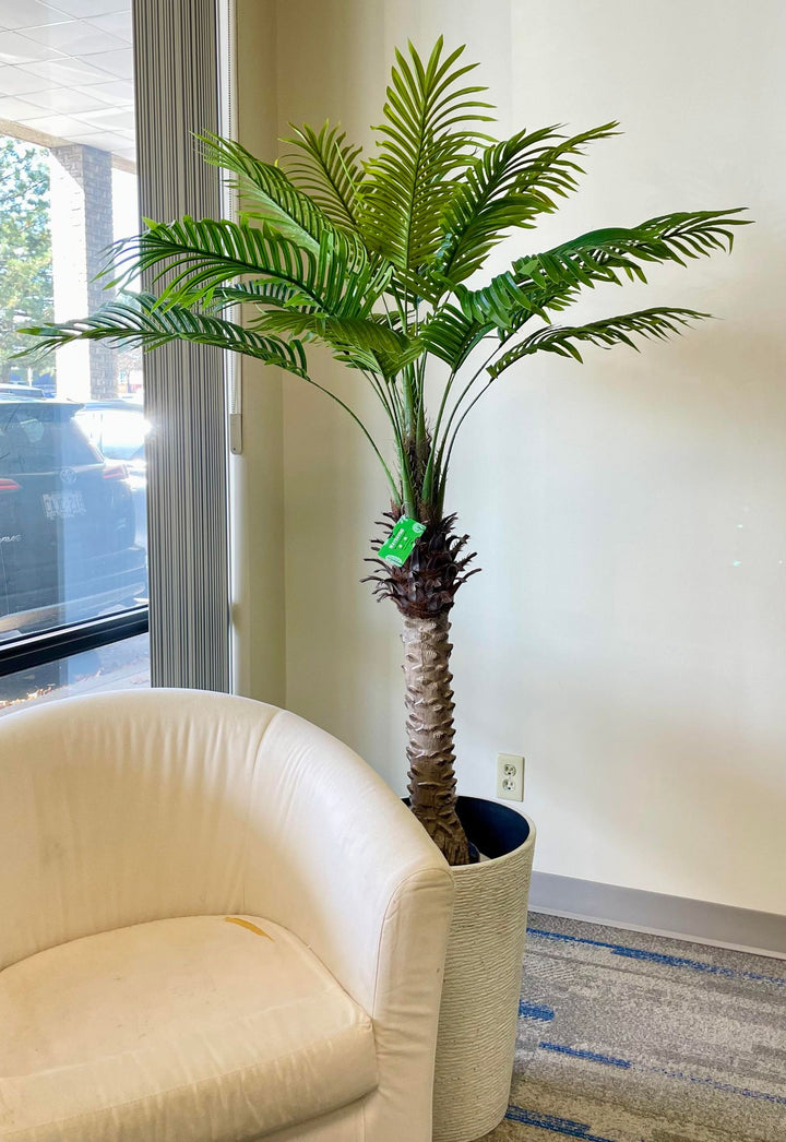 Realistic artificial palm tree placed next to a beige chair, bringing natural vibes to any interior design space.