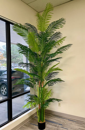 Artificial tall palm tree in a black pot placed beside a large window, ideal for enhancing office or home decor with a tropical vibe.