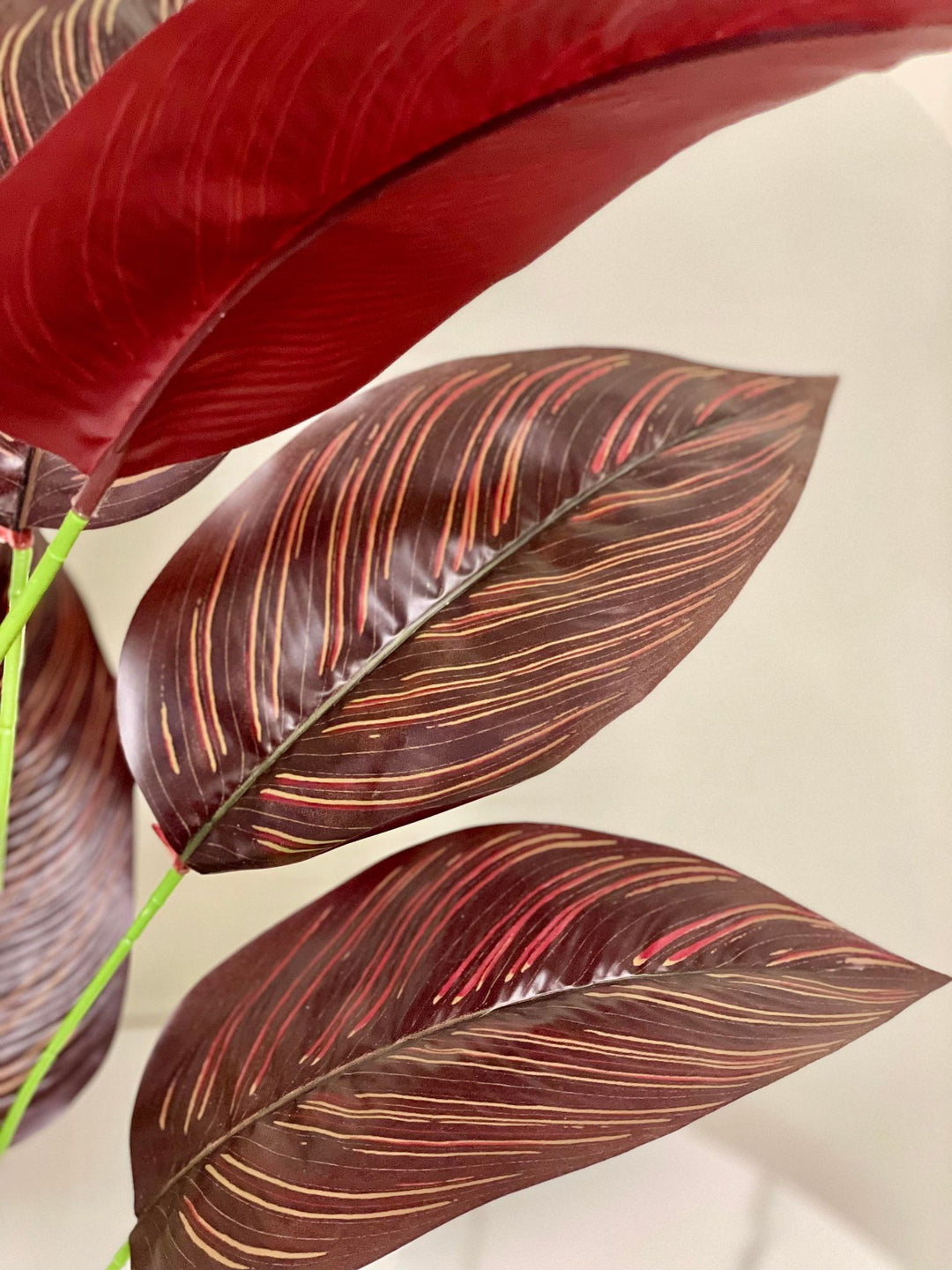 Close-up of artificial dark red and brown tropical leaves with detailed veining, bringing a vibrant and exotic flair to any indoor setting.