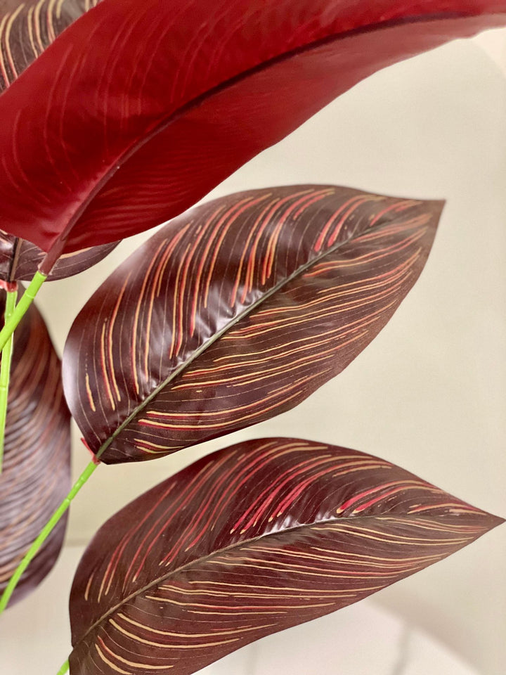 Close-up of artificial dark red and brown tropical leaves with detailed veining, bringing a vibrant and exotic flair to any indoor setting.