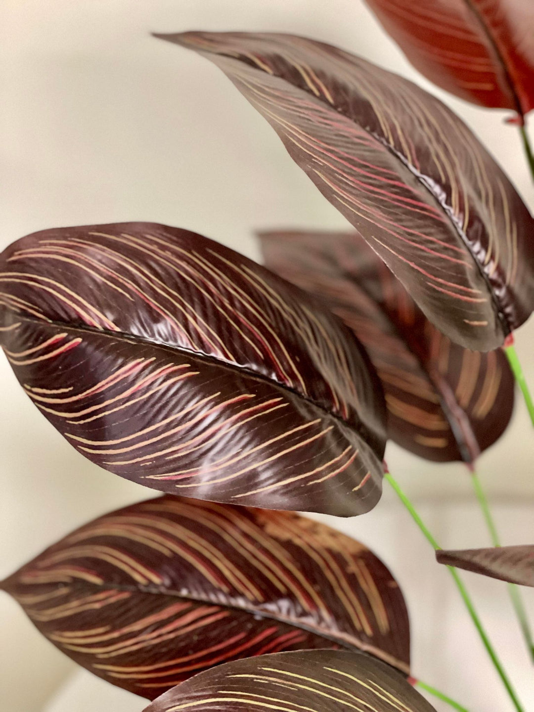 Close-up of artificial dark red and brown tropical leaves with detailed veining, bringing a vibrant and exotic flair to any indoor setting.